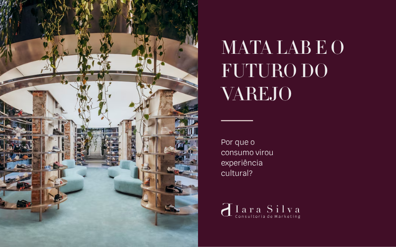 Interior da loja Mata Lab, um espaço moderno com conceito biofílico, onde estantes circulares exibem diversos modelos de calçados no centro do ambiente. Acima delas, uma estrutura metálica suspensa sustenta plantas pendentes e vegetação abundante. O espaço possui grandes janelas, iluminação natural, poltronas em tons claros e prateleiras com roupas nas laterais, criando uma atmosfera sofisticada e integrada à natureza.